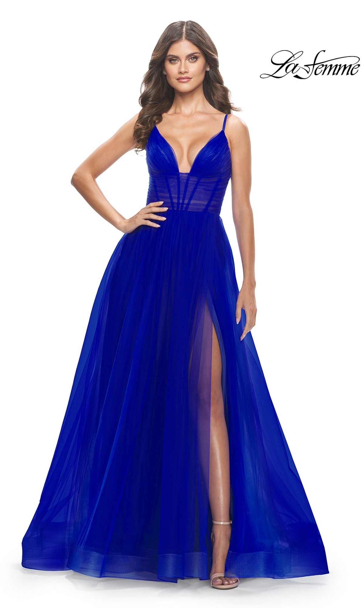 Woman in a sleeveless, deep blue Sheer-Waist La Femme Long Prom Ball Gown 31147 with a deep V-neckline, sheer bodice, and high slit stands with one hand on her hip.